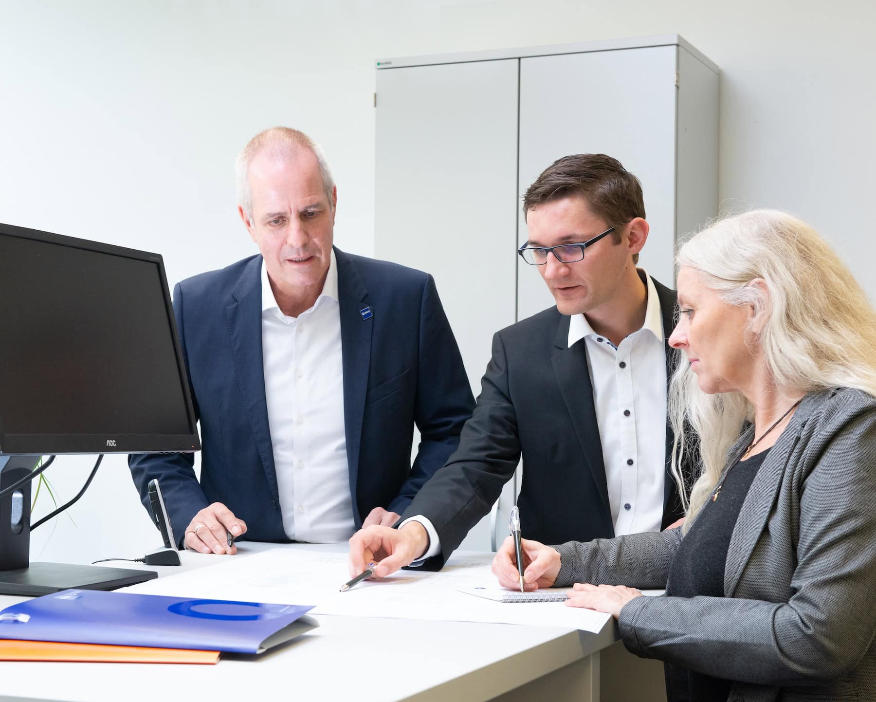 Drei QUBUS-Mitarbeiter besprechen Unterlagen am Schreibtisch