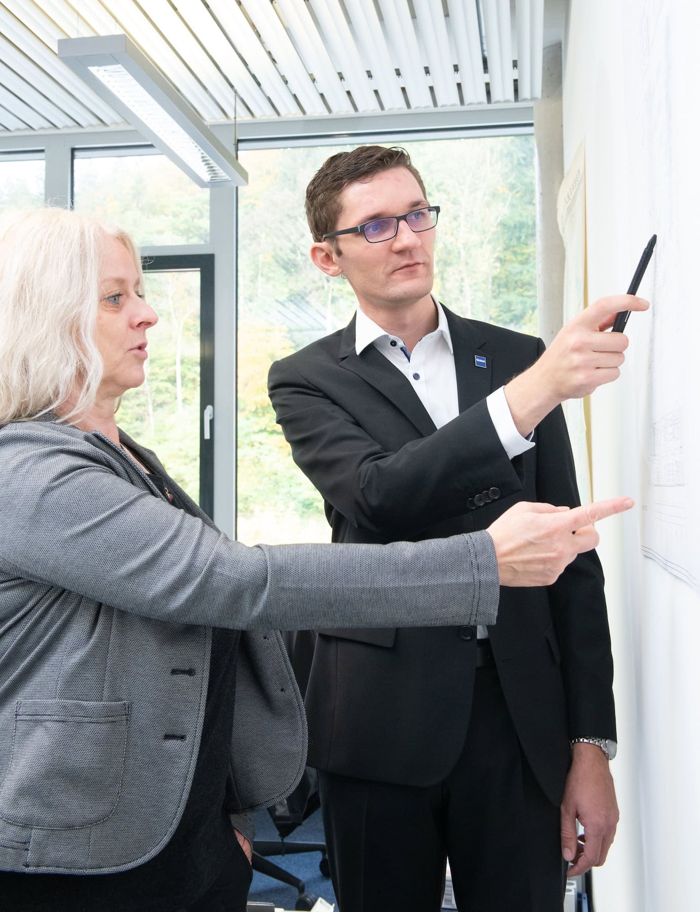 Zwei Mitarbeiter besprechen einen Plan an der Wand